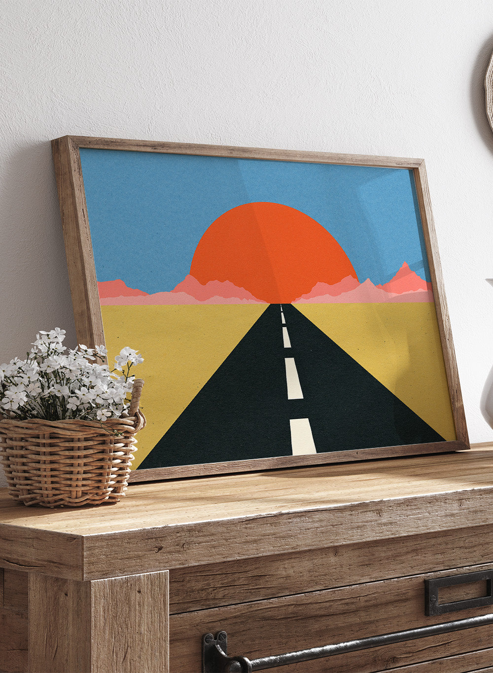 Simplified illustration of a road leading to a large red sun in a blue sky. Road To Sun by Rosi Feist is a modern landscape art print featuring a minimalist desert road, bold sunset colors, and contemporary graphic poster design.
