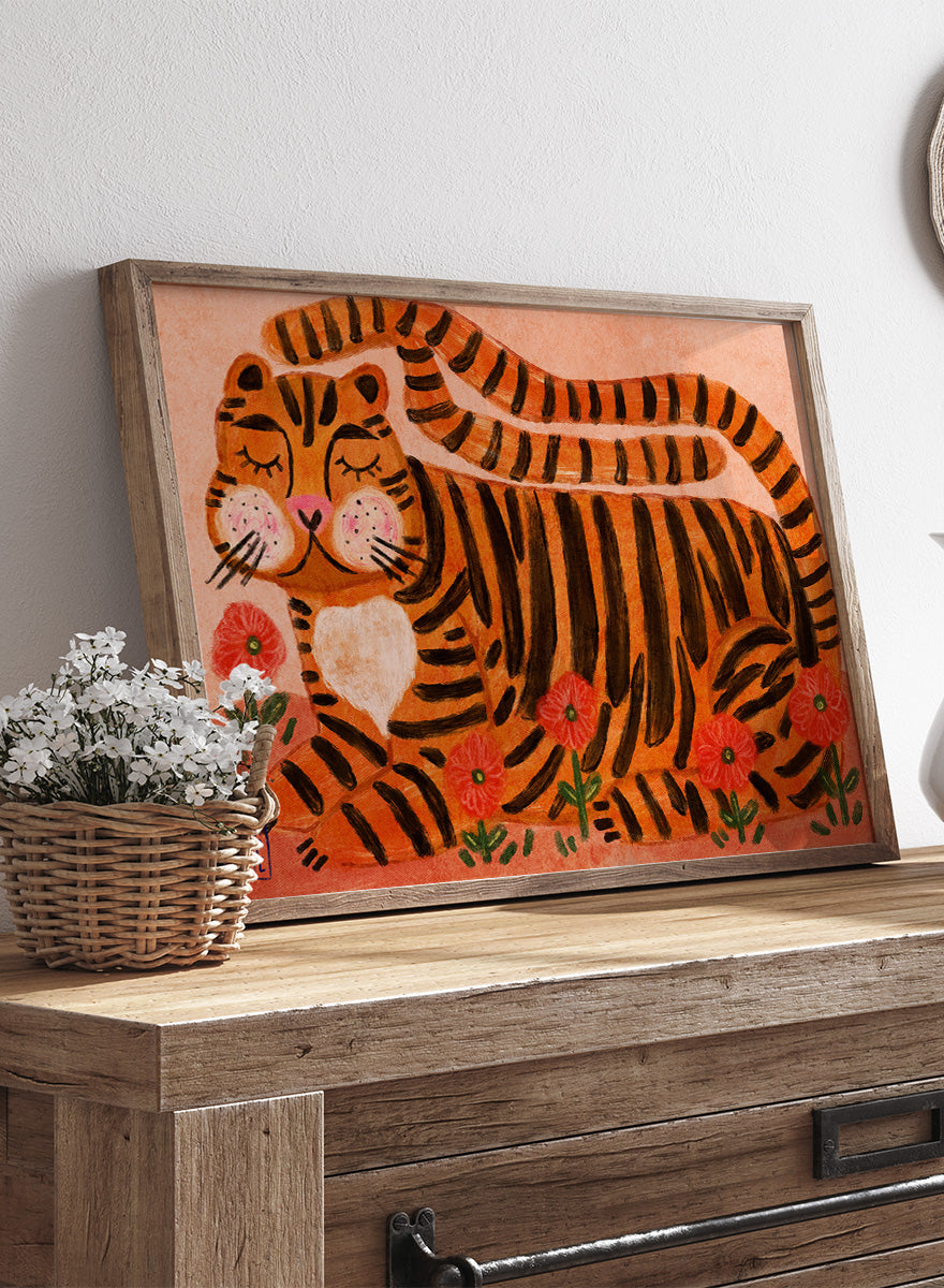 A framed art print featuring a stylized orange and black striped tiger lying among red flowers on a peach background. Playful tiger animal art print by Dirkie Nell with bold orange stripes, red poppies, and a warm peach background. Shop this cheerful piece today.