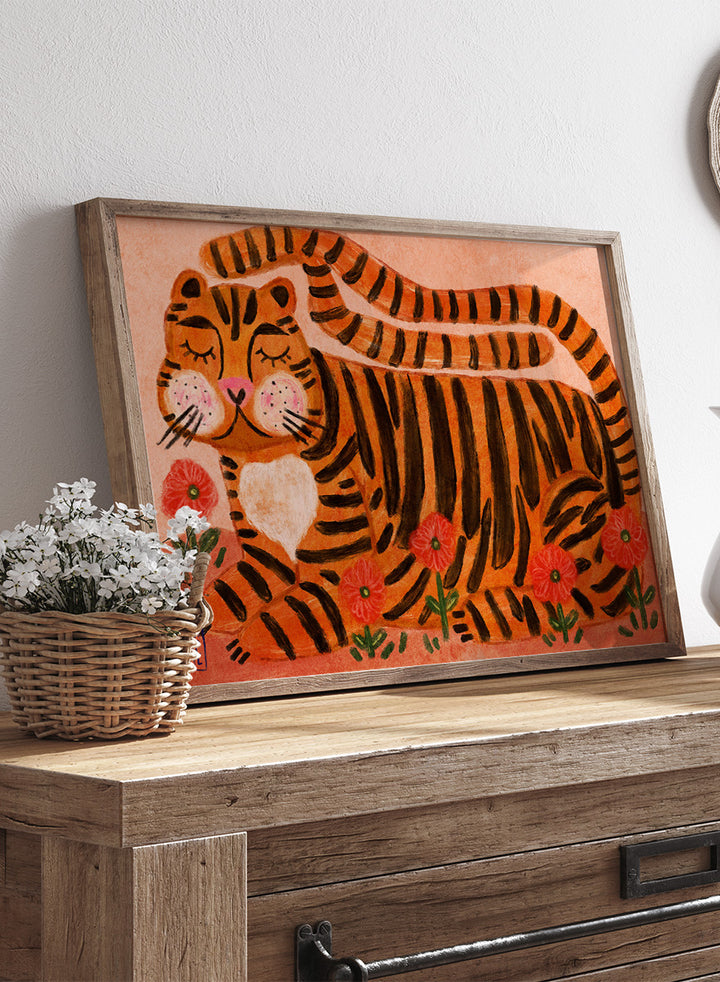 A framed art print featuring a stylized orange and black striped tiger lying among red flowers on a peach background. Playful tiger animal art print by Dirkie Nell with bold orange stripes, red poppies, and a warm peach background. Shop this cheerful piece today.