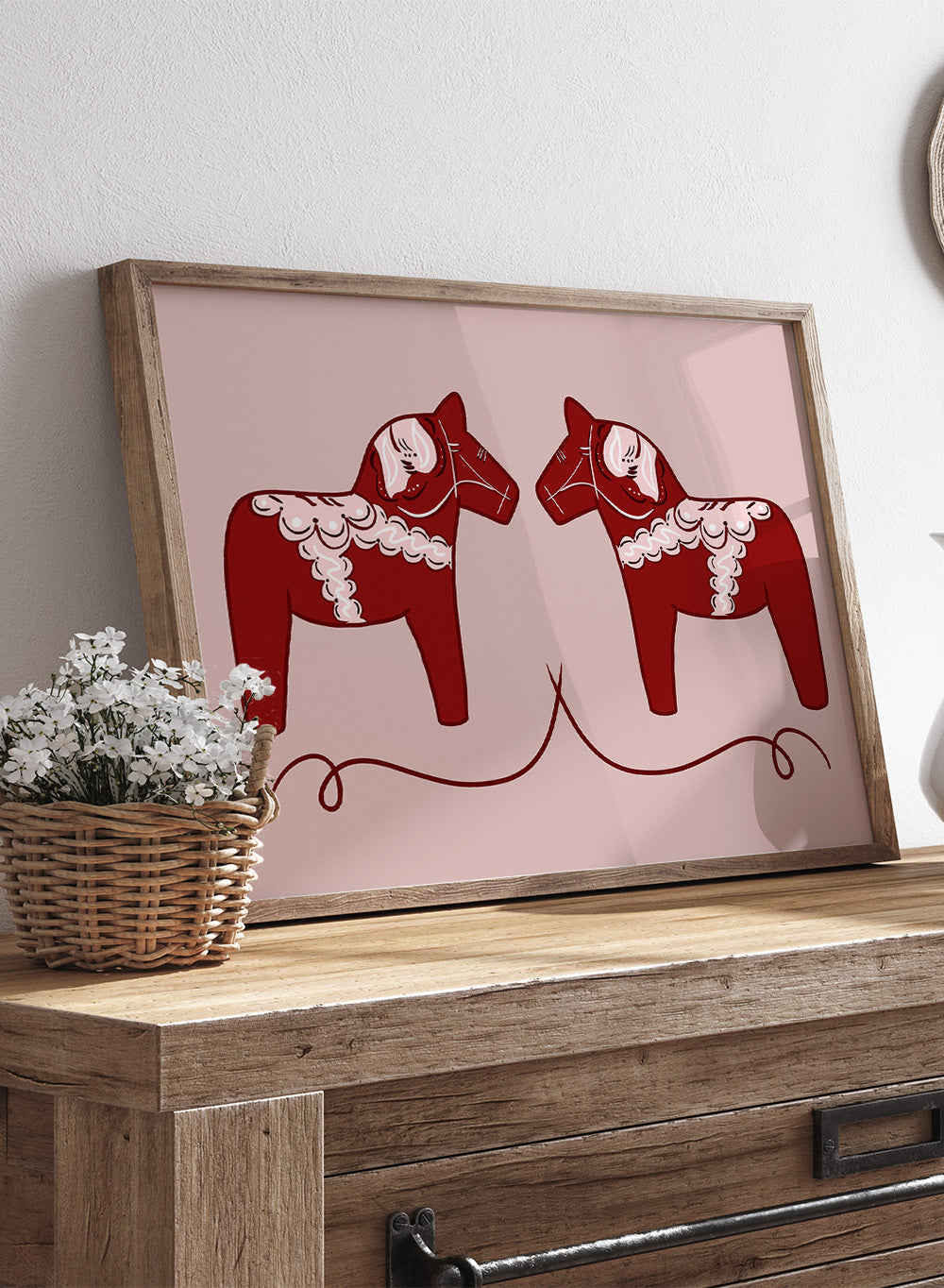 Two red Dala horse figures with white patterns on a pink background. Nordic Horses Twins by Athene Fritsch is a Scandinavian folk art illustration art print featuring Swedish Dala horses, bold red color, and modern wall art design.
