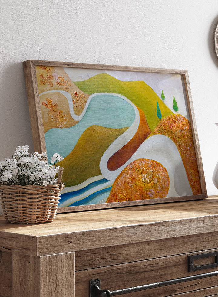 A framed abstract landscape painting featuring winding light blue and white river-like curves, green hills, and textured orange-brown foreground shapes. Shop Serene Valley Path by Angeles M. Pomata, a colorful landscape art print featuring a winding path, river, rolling hills, and warm earthy tones.
