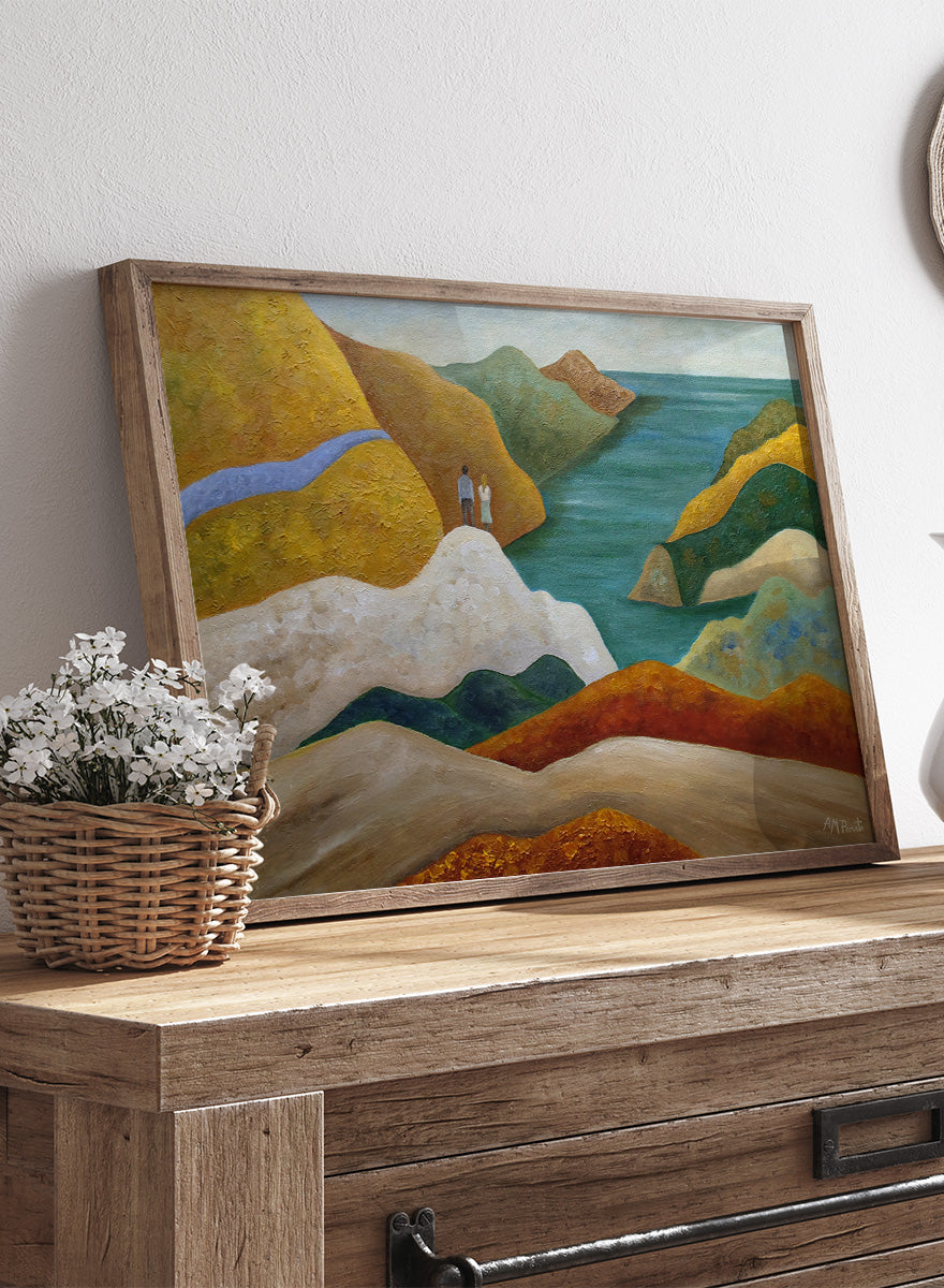 A framed landscape painting featuring stylized coastal cliffs, hills, and a body of water in earthy yellow, orange, green, blue, and white tones. Shop Couple Overlooking Coastal View by Angeles M. Pomata, a coastal landscape and figurative art print featuring a couple, rolling hills, and a blue sea view.