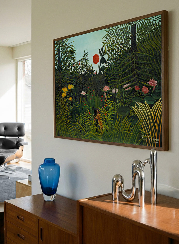 A framed art print depicting a lush, stylized jungle scene with dense green foliage, a small figure, and a bright red sun against a pale sky. Virgin Forest with Sunset by Henri Rousseau is a vintage jungle art print featuring lush tropical foliage, bright flowers, wildlife, and a red setting sun.