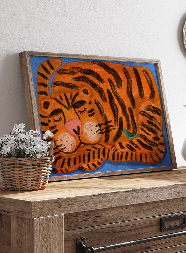 A framed painting of a sleeping tiger on a blue background. The tiger is orange with bold black stripes, has a pink nose and cheeks, and a small green bird near its side. A framed painting of a sleeping tiger on a blue background. The tiger is orange with bold black stripes, has a pink nose and cheeks, and a small green bird near its side. 