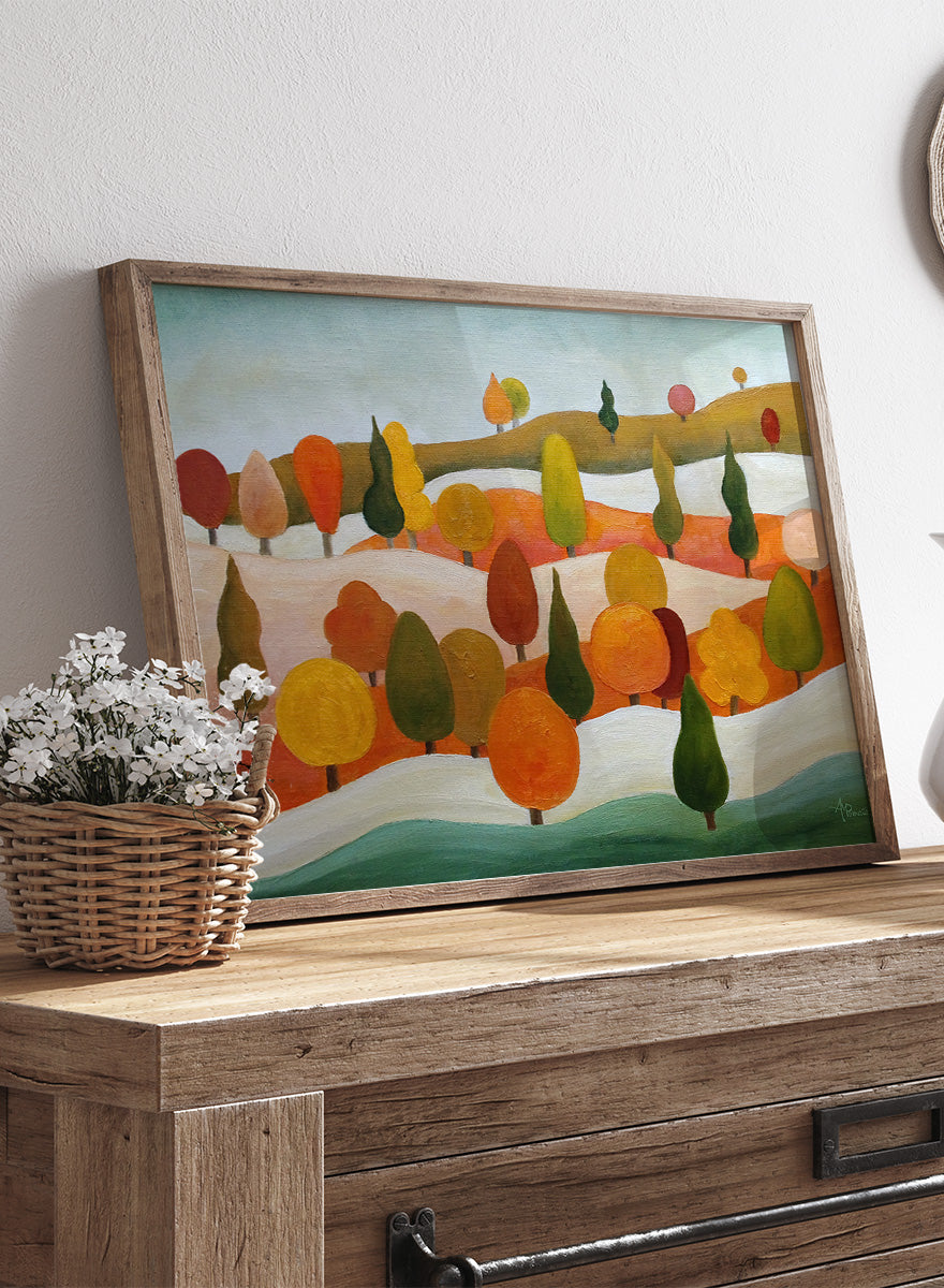 A framed landscape art print featuring stylized trees in autumn colors on rolling hills under a pale sky. Shop Colorful Autumn Hills by Angeles M. Pomata, an autumn landscape art print featuring rolling hills, stylized trees, and warm fall color.