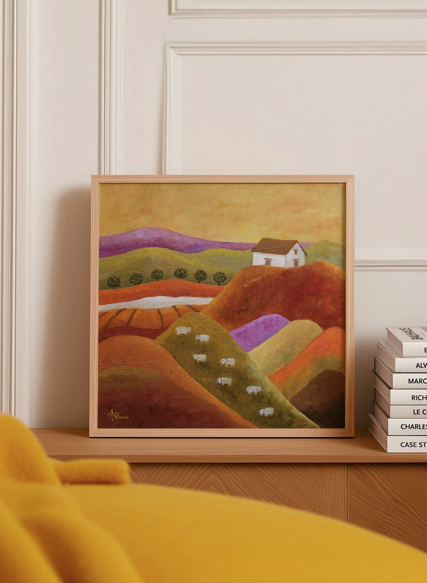 A framed landscape painting featuring rolling hills in warm earth tones, purple and green valleys, a small white house, and white sheep. Shop Pastoral Hills With Sheep by Angeles M. Pomata, an autumn countryside art print featuring rolling hills, grazing sheep, a white farmhouse, and warm earthy tones.