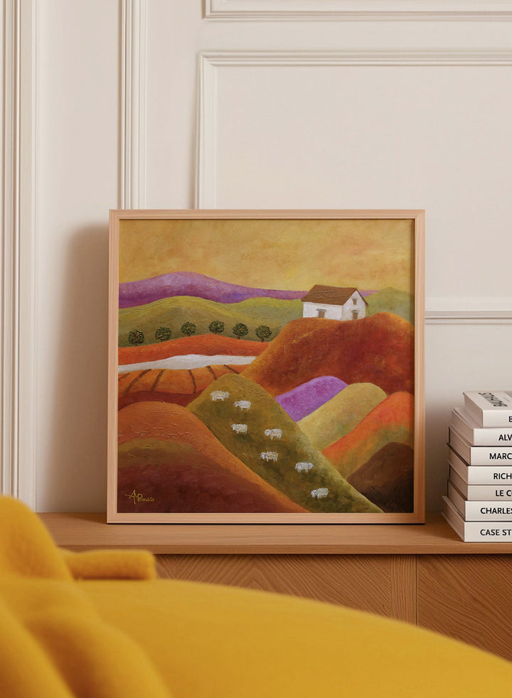 A framed landscape painting featuring rolling hills in warm earth tones, purple and green valleys, a small white house, and white sheep. Shop Pastoral Hills With Sheep by Angeles M. Pomata, an autumn countryside art print featuring rolling hills, grazing sheep, a white farmhouse, and warm earthy tones.
