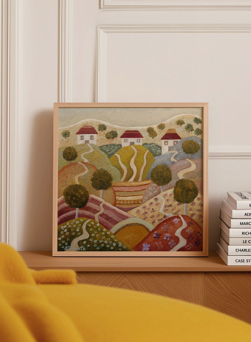 A framed landscape painting featuring stylized rolling hills, winding paths, small houses with red roofs, and trees. Shop Charming Hillside Village by Angeles M. Pomata, a colorful countryside art print featuring winding paths, red-roof houses, flowering fields, and warm autumn tones.