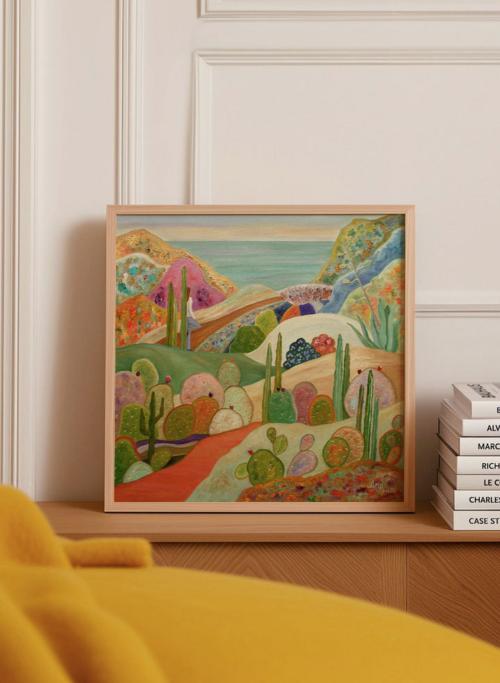 A framed colorful landscape painting featuring stylized cacti, hills, and a coastal scene. Shop Colorful Desert Yoga View by Angeles M. Pomata, a colorful desert landscape art print featuring cacti, rolling hills, a yoga figure, and coastal views.