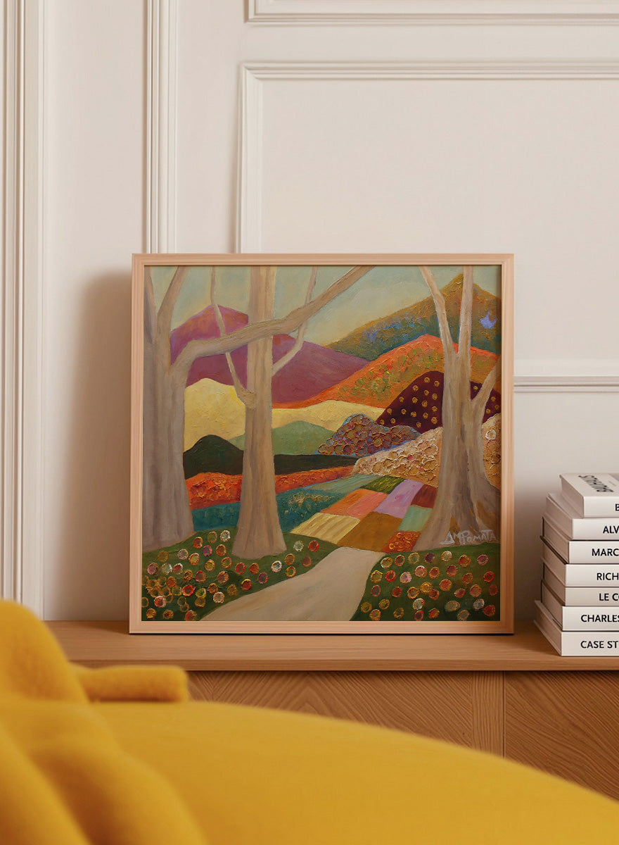 A framed landscape painting featuring stylized trees, a winding path, patchwork fields, and mountains in warm earthy tones. Shop Colorful Field Path by Angeles M. Pomata, an autumn landscape art print featuring a winding path, textured fields, flowers, and rolling countryside.