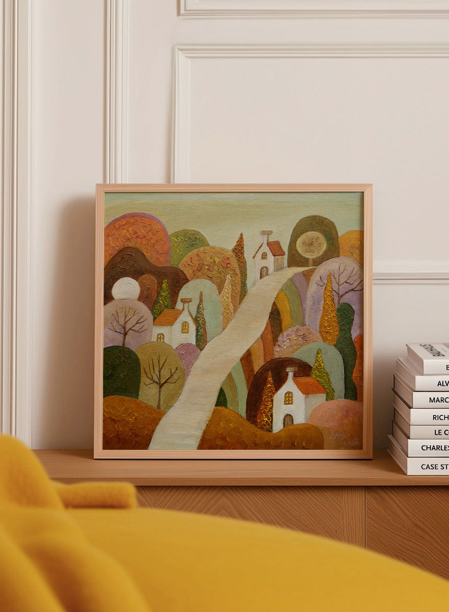 A framed landscape painting featuring stylized white houses, a winding cream path, and rolling hills in earthy tones of brown, orange, green, and purple. Shop Whimsical Village Path by Angeles M. Pomata, an autumn landscape art print featuring a winding road, white village houses, rounded hills, and warm earthy tones.