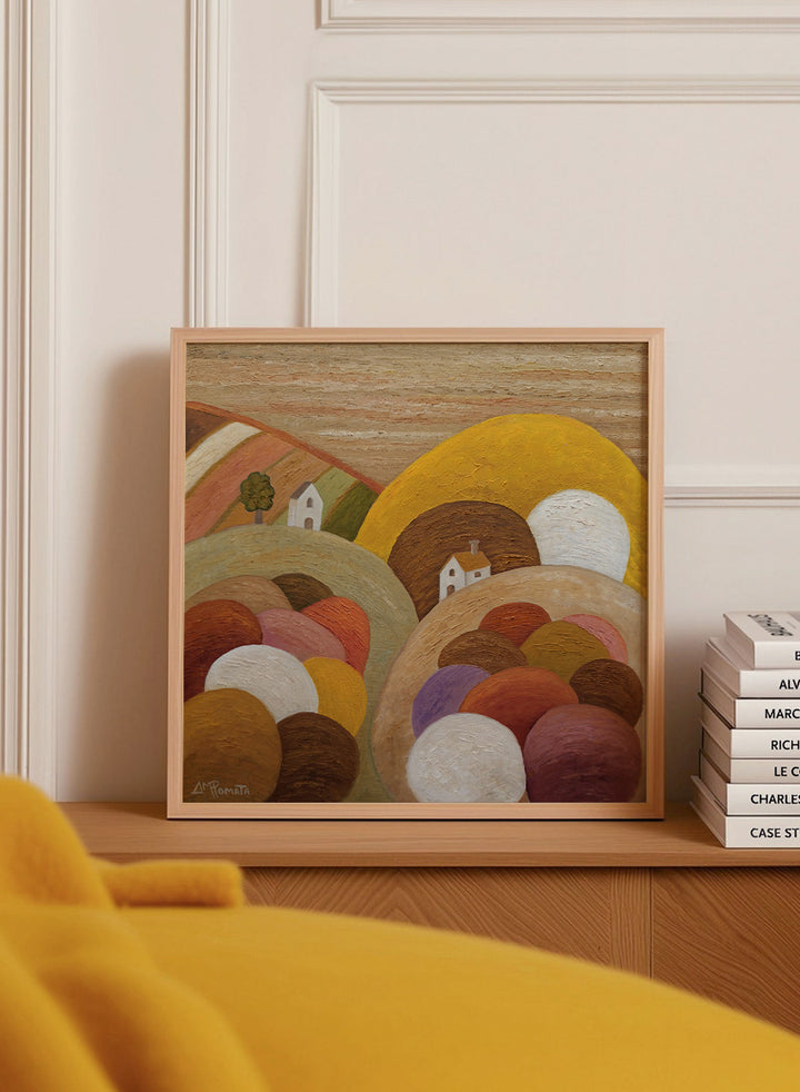 A framed abstract landscape painting featuring stylized hills, rolling forms, small houses, and a large yellow circular shape. Shop Colorful Hillside Village by Angeles M. Pomata, an autumn landscape art print featuring rounded hills, tiny white houses, earthy tones, and rich oil texture.