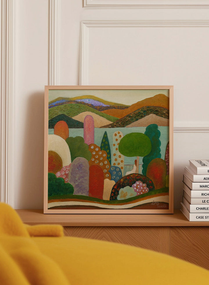 A framed landscape painting featuring stylized hills, trees, and abstract shapes in earthy tones of green, brown, orange, red, blue, and purple. Shop Vibrant Whimsical Landscape by Angeles M. Pomata, a colorful landscape art print with layered hills, patterned trees, and a soft dreamlike feel.