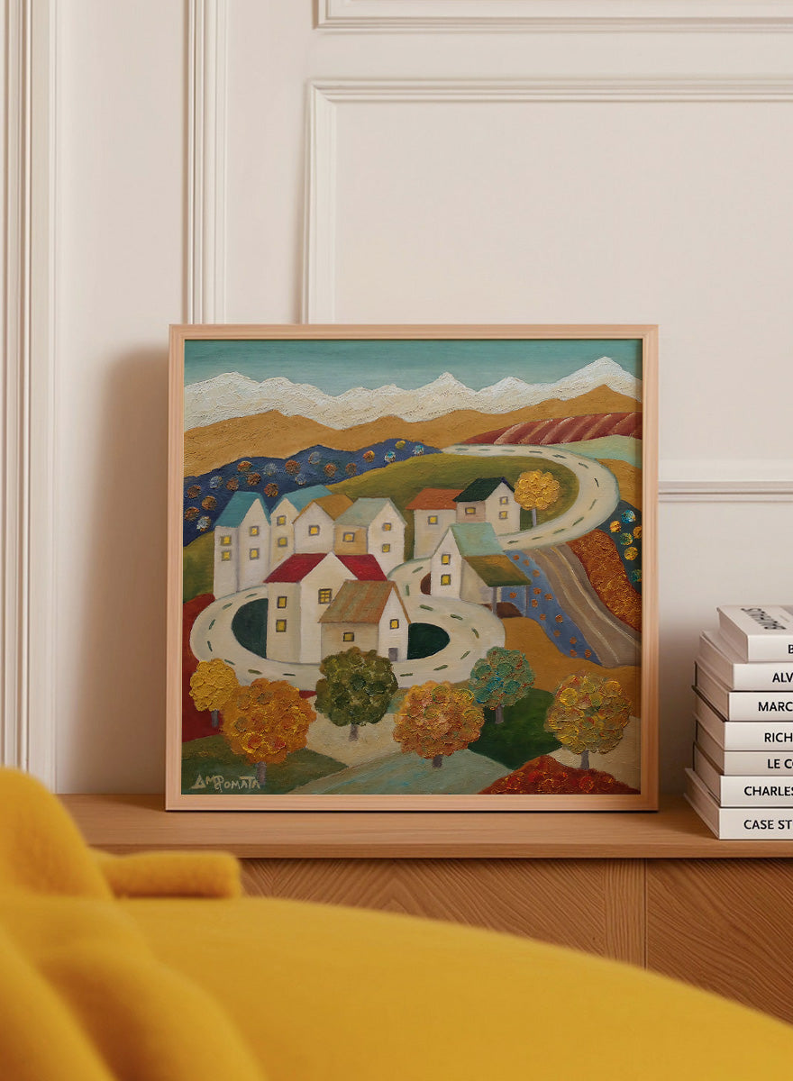 A framed folk-art style landscape painting depicting a village with white houses, winding roads, colorful trees, and mountains under a blue sky. Shop Autumn Road Village by Angeles M. Pomata, a colorful autumn landscape art print featuring a winding road, white village houses, fall trees, and distant mountains.