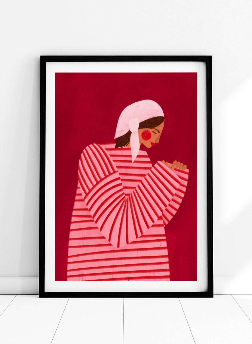 A framed art print featuring a stylized illustration of a woman in a pink and red striped top and white headscarf against a deep red background. Serene Praying Woman by Bea Müller portrait art print featuring a reflective woman in a pink striped dress against a rich red background.