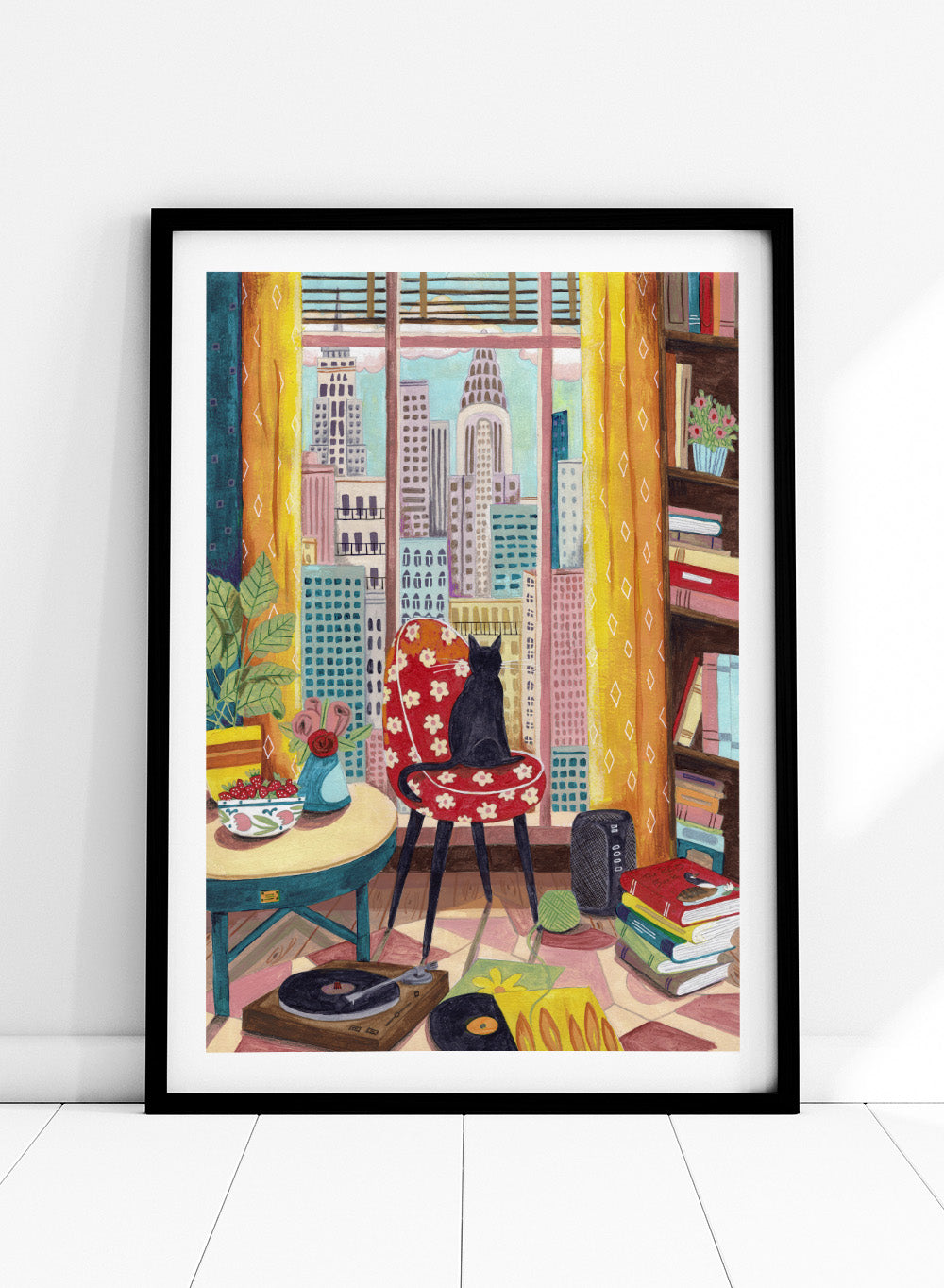 Colorful interior scene with a cat on a chair, books, and cityscape view. Black Cat City View by Caroline Bonne Müller is a fine art print and wall poster of a black cat by a window with city skyline and colorful interior.