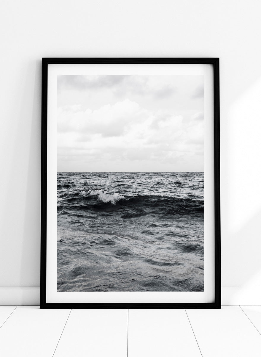 Black and white photographic art print of ocean waves under a cloudy sky. Endless Waves by Shot by Clint black-and-white ocean photography print featuring rolling water, textured surf, cloudy skies, and dramatic coastal movement.