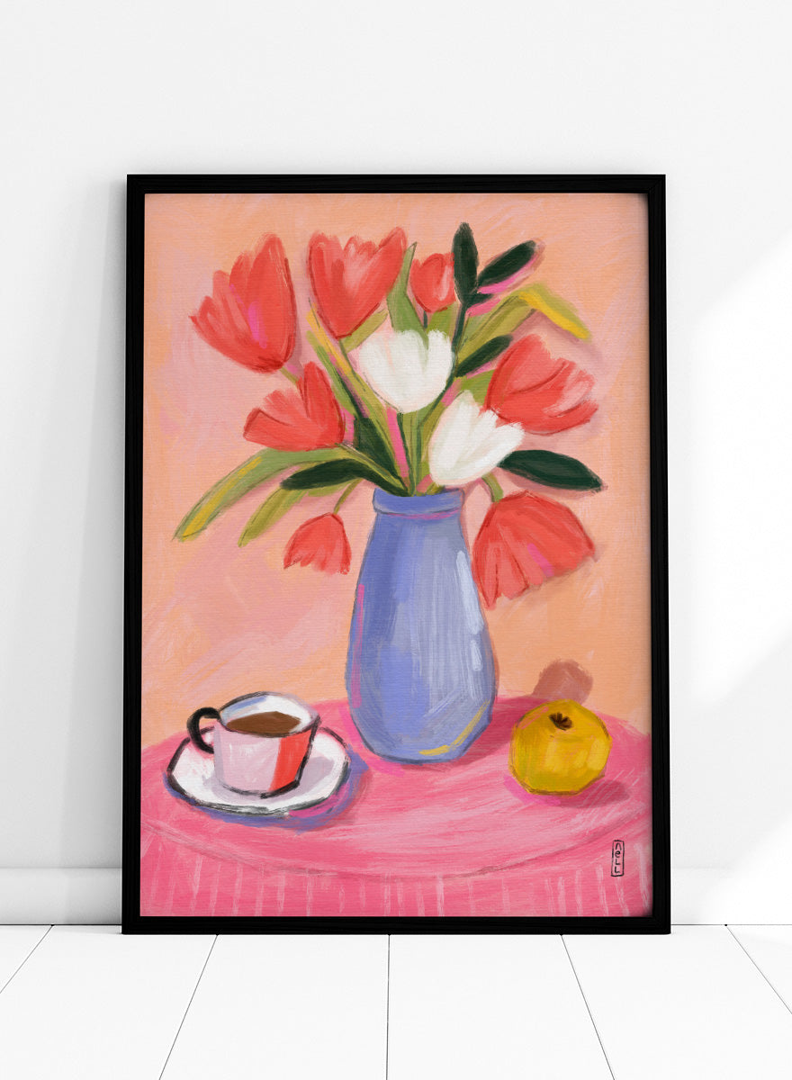 A still life painting of a bouquet of red and white tulips in a blue vase, set on a pink tablecloth next to a cup of coffee and a yellow fruit, against a peach background. Shop Fresh Tulips and Coffee by Dirkie Nell, a colorful floral still life art print featuring tulips, coffee, a blue vase, and warm pink and peach tones.