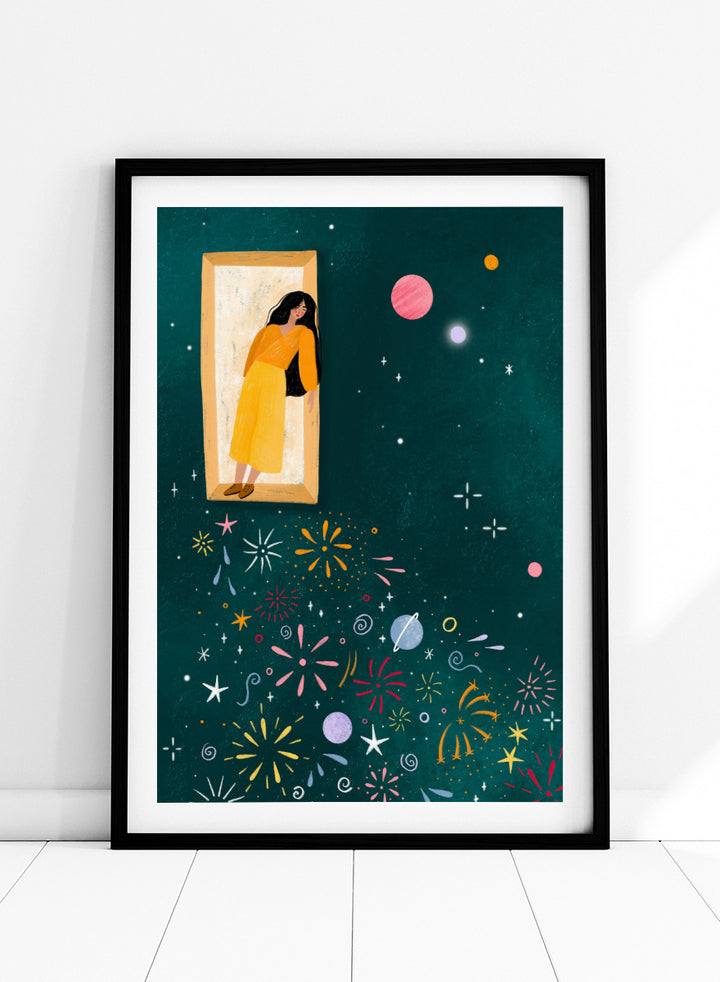 A framed art print featuring a whimsical illustration of a woman in a yellow dress standing in a mirror, with her reflection spreading colorful fireworks and space-themed motifs like planets and stars across a dark teal background. Shop Girl and Cosmic Fireworks by Bea Müller, a figurative wall art print poster featuring a woman, planets, stars, and colorful cosmic fireworks in deep green tones.
