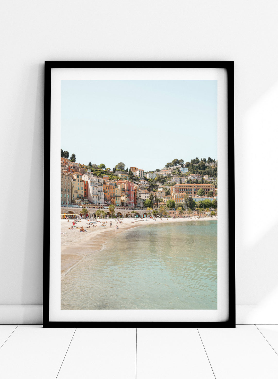 Coastal town with colorful buildings and a beach. Sunny Mediterranean Coast by Henrike Schenk is a coastal photography print featuring turquoise water, pastel buildings, Mediterranean beach scenery, and travel wall art.