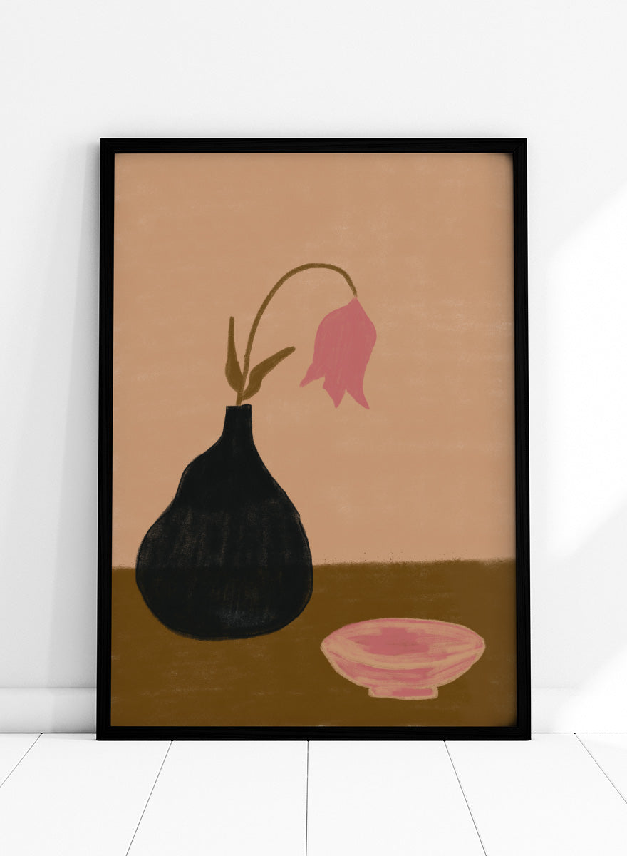 A minimalist still life painting featuring a black pear-shaped vase with a single drooping pink flower, alongside a pink bowl, set against a warm beige background and a brown tabletop. Minimal Pink Still Life by The Art Concept still life art print featuring a black vase, drooping pink flower, small bowl, and warm earthy tones.