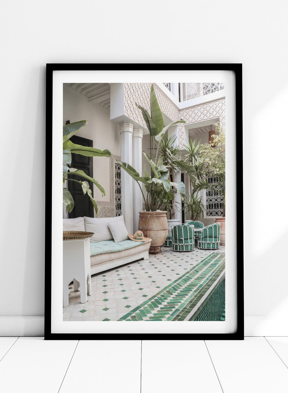 Outdoor patio with white sofa, green chairs, and potted plants in a decorative courtyard. Moroccan Riad Courtyard Oasis by Henrike Schenk is a Morocco photography print of a riad courtyard with tropical plants, tilework, and interior decor.