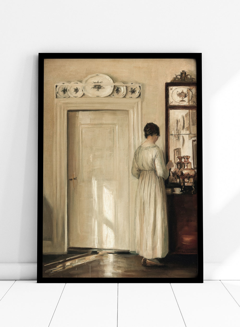 Woman in a white dress standing in a room with a door and shelves filled with items. Woman Making Tea by Carl Holsøe is a vintage Danish interior art print featuring Scandinavian home interiors, muted tones, natural light, and a woman preparing tea.