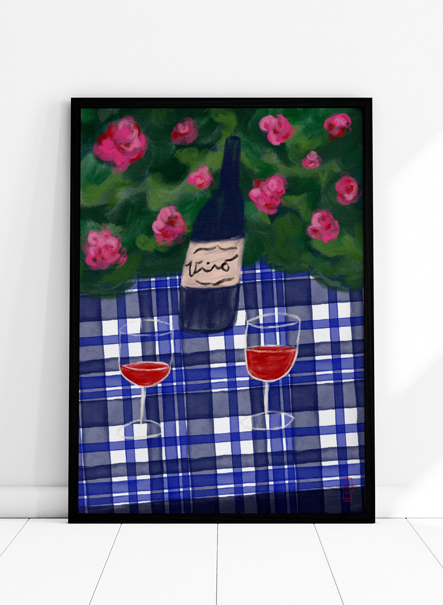 A painted still life scene featuring a dark wine bottle labeled 'vino' on a blue-and-white plaid tablecloth, with two glasses of red wine and pink flowers against a green background. Shop Garden Wine Picnic by Dirkie Nell, a colorful still life art print featuring red wine, blue gingham, pink roses, and a warm summer garden mood.