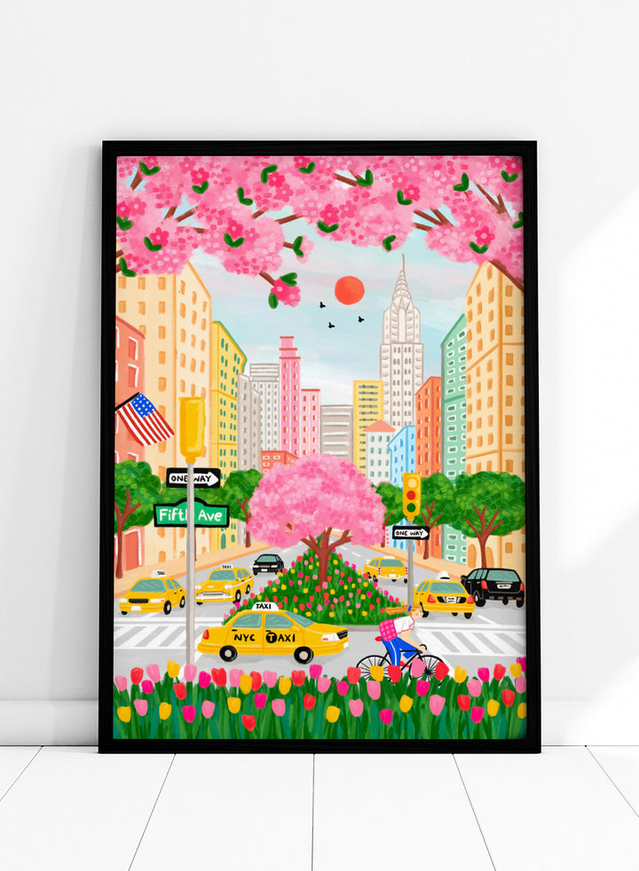 A colorful illustrated city street scene with pink cherry blossoms overhead, yellow NYC taxis, tall buildings, a bicycle with a pink basket, flowers in the foreground, and street signs including Fifti Ave. Shop NYC Cherry Blossoms by Nidhi Kachhadiya, a colorful New York City wall art print with Fifth Avenue, yellow taxis, pink blossoms, and spring city charm.