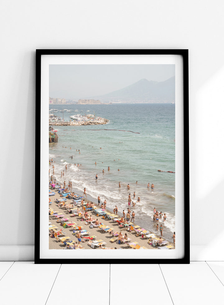 Beach scene with people and umbrellas near a body of water with mountains in the background. Summer Beach Mountain View by Henrike Schenk is a Mediterranean beach photography print featuring coastal views, mountains, ocean scenery, and summer travel.
