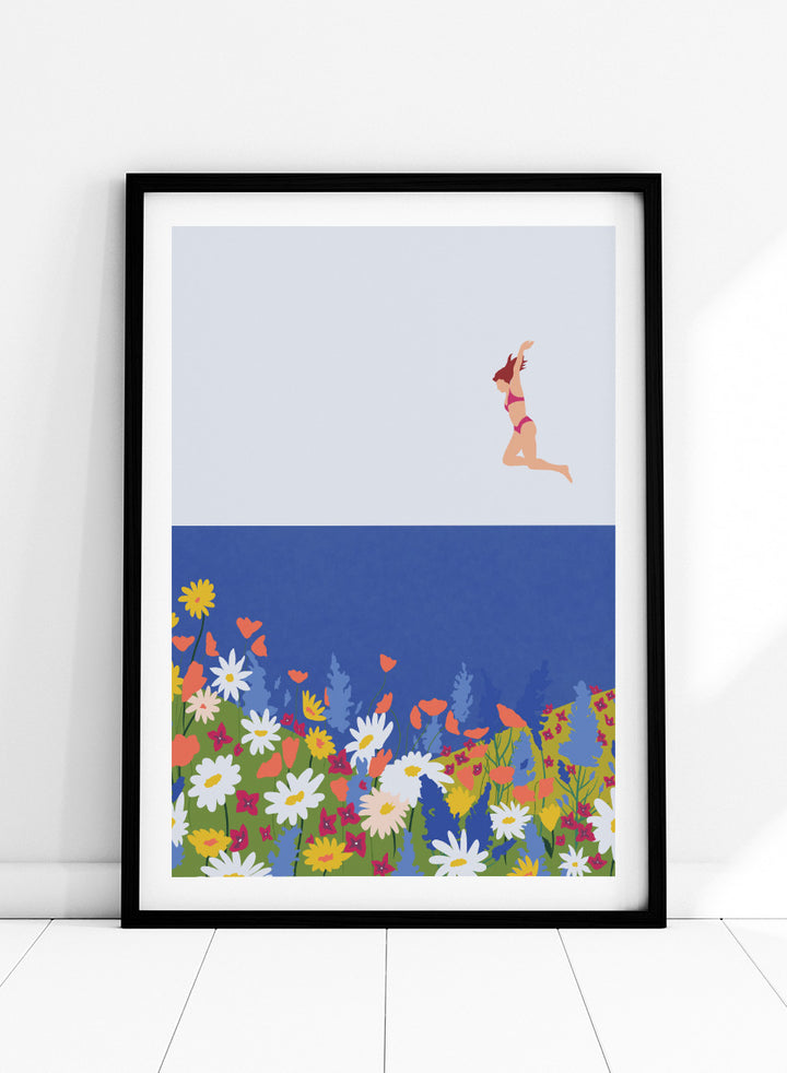A framed art print featuring a minimalist illustration of a woman in a pink bikini jumping into a blue sea with a colorful wildflower meadow below. Wildflower Summer Jump art print by Ceyda Alasar features a joyful figure above colorful blooms, bringing playful summer energy to your walls.