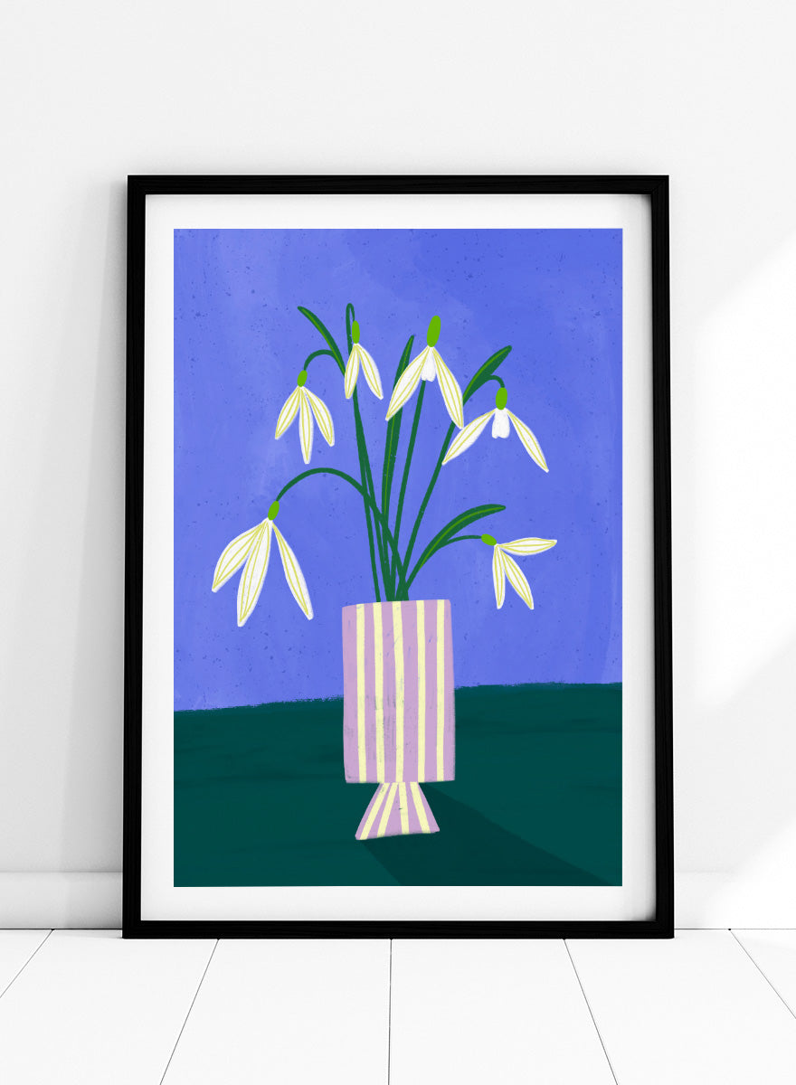 A framed art print featuring a stylized illustration of white snowdrops with green stems in a lavender and cream striped vase, set against a blue and dark green background. Snowdrops in Striped Vase by Bea Müller fine art print featuring white snowdrops, a lilac striped vase, and a deep blue background.