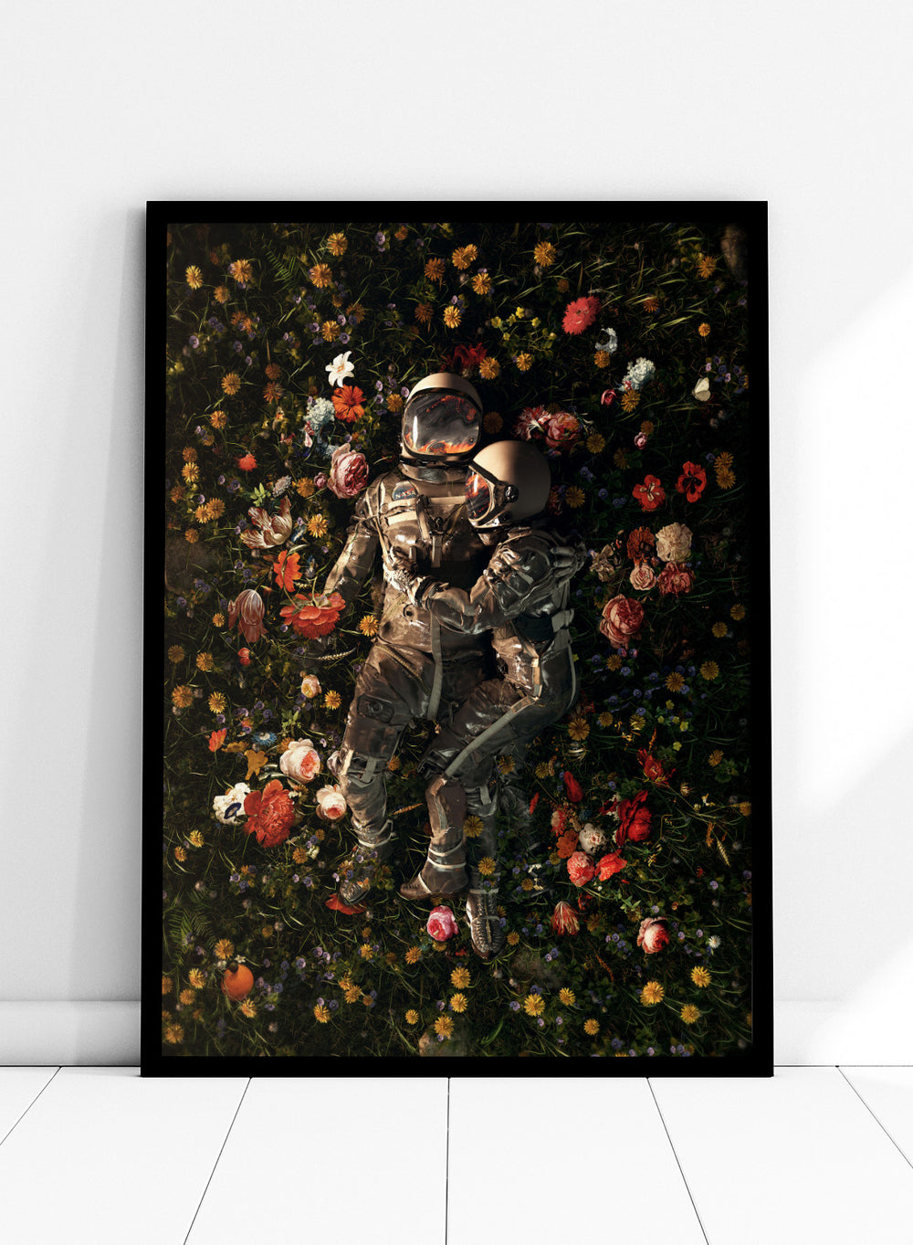 Astronaut lying on a bed of flowers with a dark background. Cosmic Couple Bloom by Nicebleed is a surreal astronaut floral art print featuring two astronauts in a field of flowers, modern aesthetic wall poster.