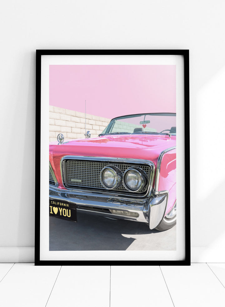 Pink vintage car with 'I ❤️ YOU' license plate against a pink sky. P.S. I Love You by Tom Windeknecht is officially licensed photography featuring a vibrant pop-art style photo of a car with romantic typography. Framed or unframed.