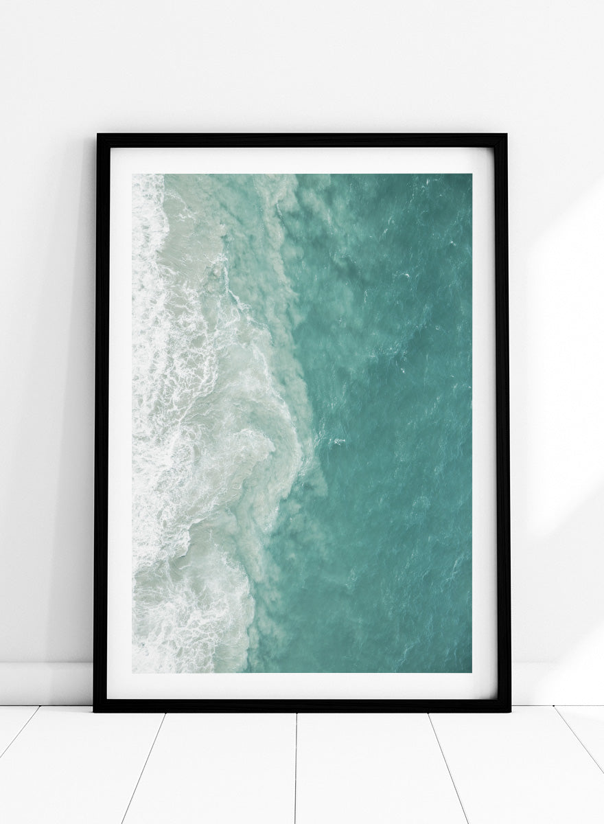 A framed aerial photograph of ocean waves, showing white foam breaking into turquoise and teal water. Ocean’s Edge by Shot by Clint aerial ocean photography print featuring turquoise water, white surf, and layered coastal movement.