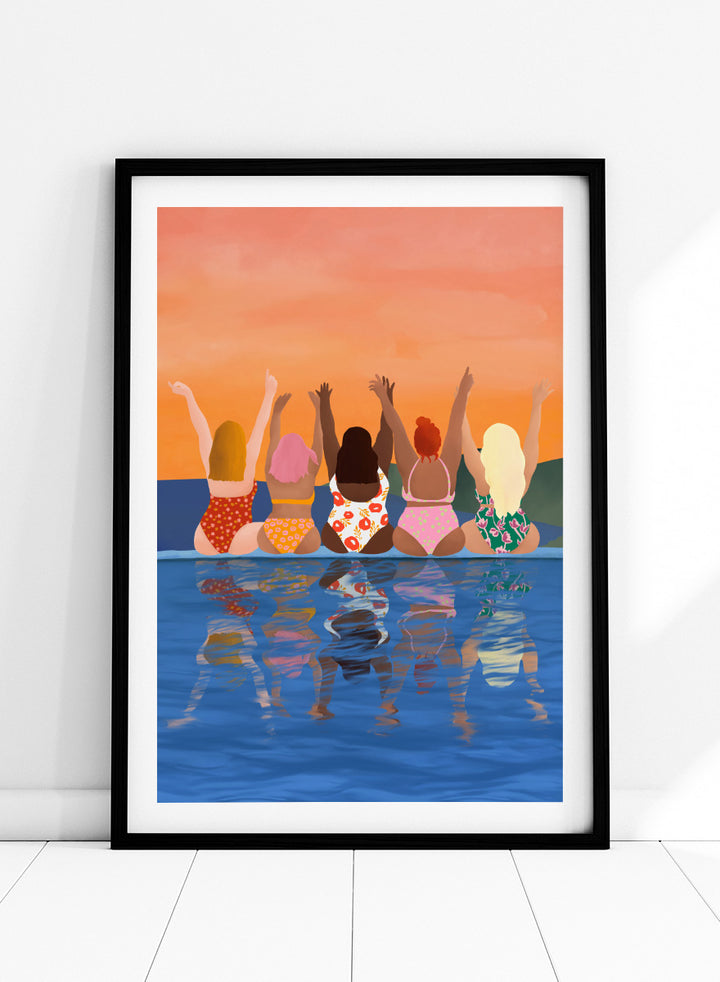 A framed art print featuring a stylized illustration of five women sitting in a pool at sunset, seen from behind as they raise their arms. The background is a warm orange sky, and the water below reflects their silhouettes. Summer Sunset Friends by Ceyda Alasar friendship art print featuring five women by the water in patterned swimsuits beneath a glowing orange sky.