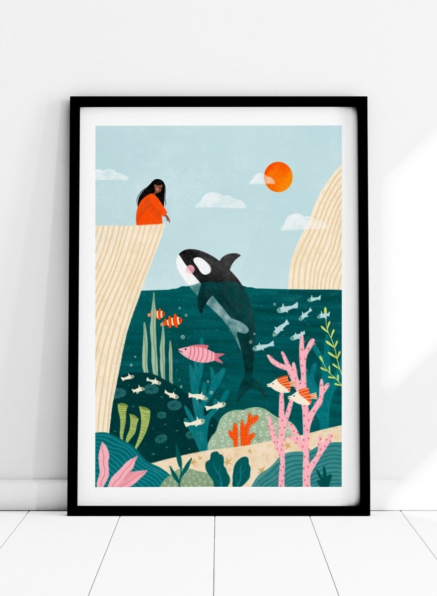 A framed art print featuring a whimsical underwater scene with an orca, coral, fish, and a woman in an orange dress standing on a cliff edge under a sun. Girl Watches Ocean Life by Bea Müller premium framed fine art print featuring a child watching an orca swim through a colorful underwater world.
