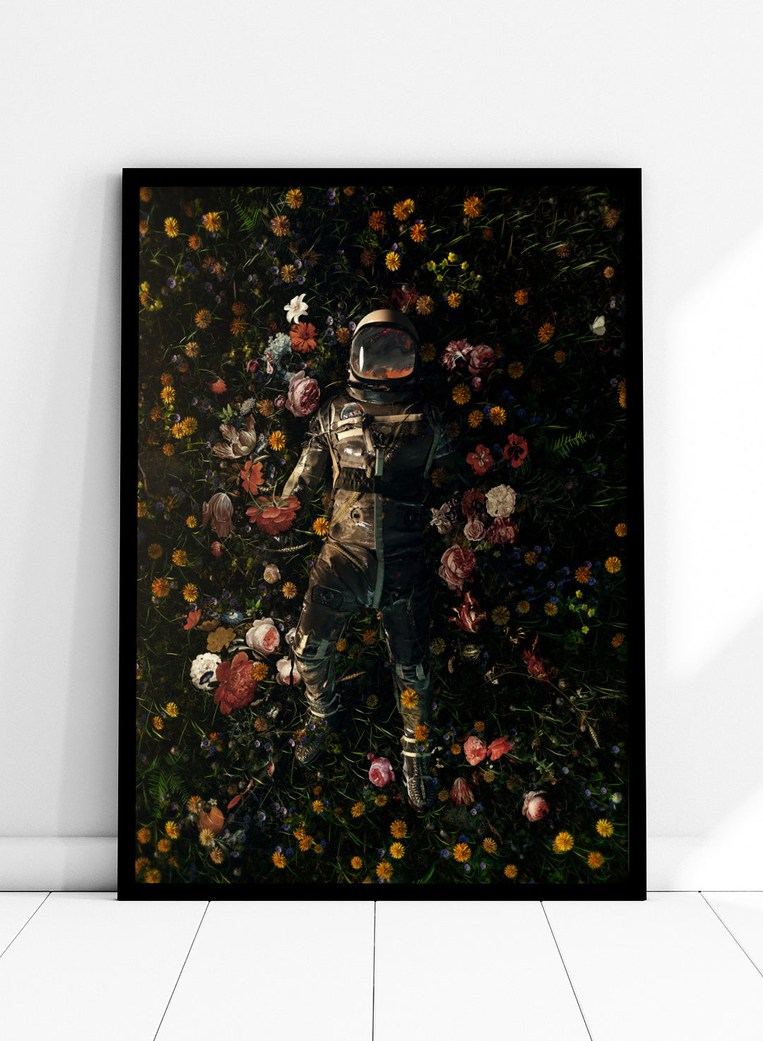 Person in a spacesuit lying on a bed of flowers with a dark background. Cosmic Floral Dream by Nicebleed is a surreal astronaut floral art print featuring a space figure surrounded by flowers, modern aesthetic wall poster.