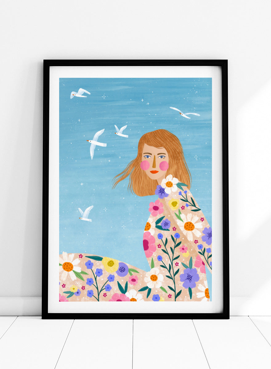 A framed art print featuring a stylized illustration of a young woman with long light brown hair, surrounded by colorful flowers and white birds against a light blue sky. ree Spirit Floral Dreams by Bea Müller floral woman art print featuring a flowing flower-covered summer dress, white birds, and a bright blue sky.