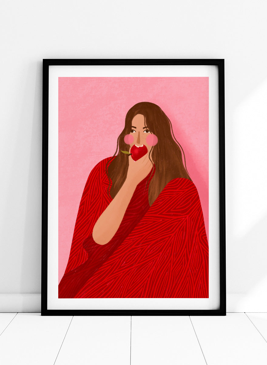A framed art print featuring a stylized illustration of a woman with long brown hair, wearing a red patterned wrap, holding a red apple to her lips, set against a pink background. Cozy Woman Apple by Bea Müller portrait art print featuring a woman eating a red apple in bold red and pink tones for colorful modern wall decor.