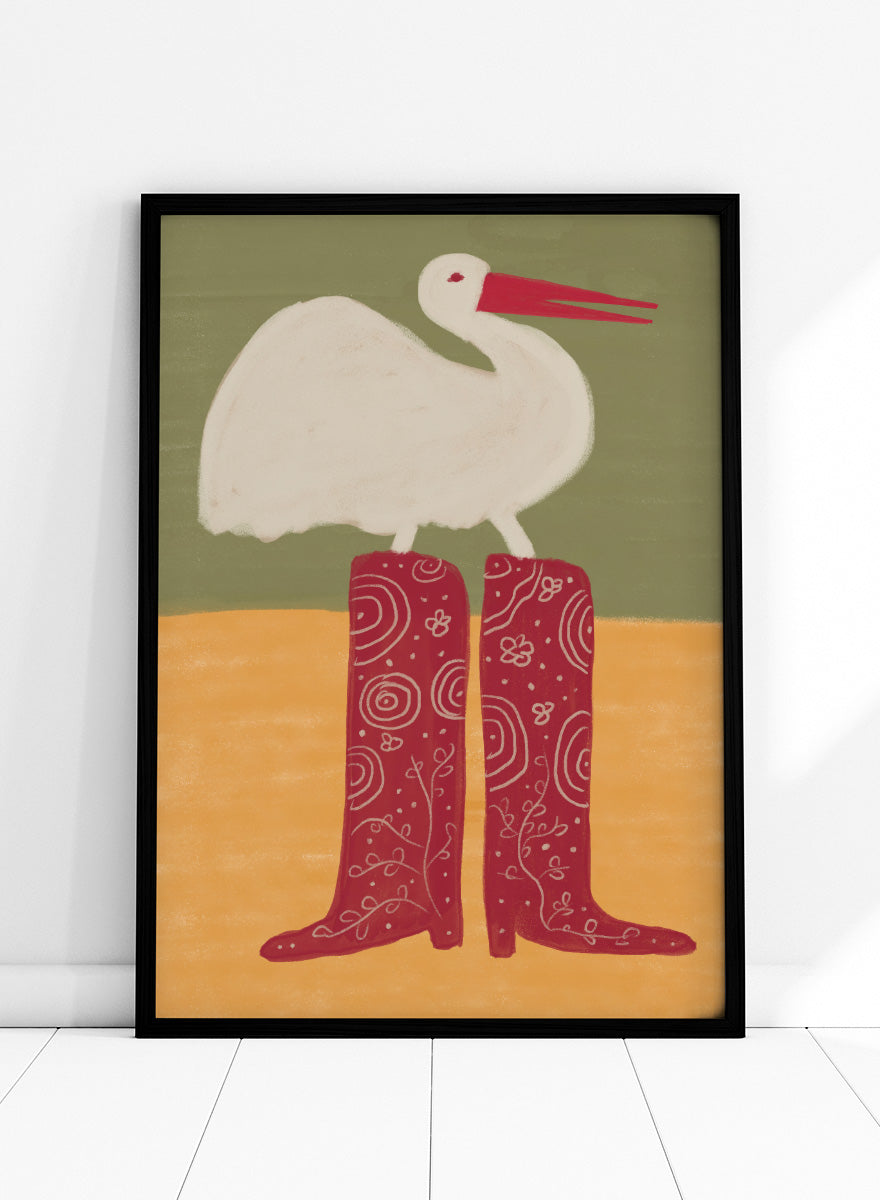 A stylized art print featuring a white stork with a red beak standing on a pair of tall red boots with white swirl patterns, set against a muted green and ochre background. Bird in Red Boots by The Art Concept playful animal art print featuring a white bird in oversized red patterned boots with soft green and ochre tones.