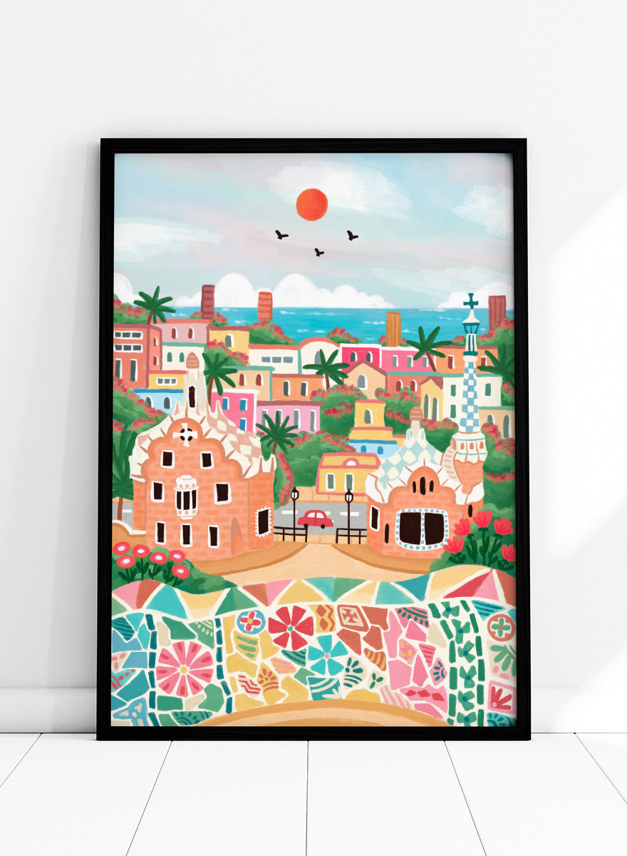 A colorful stylized illustration of a coastal town with pastel buildings, palm trees, a mosaic wall in the foreground, blue sea, and a red sun in the sky. Shop Colorful Coastal Dream by Nidhi Kachhadiya, a vibrant Barcelona wall art print inspired by Park Güell, Gaudí architecture, mosaics, and bright coastal color.
