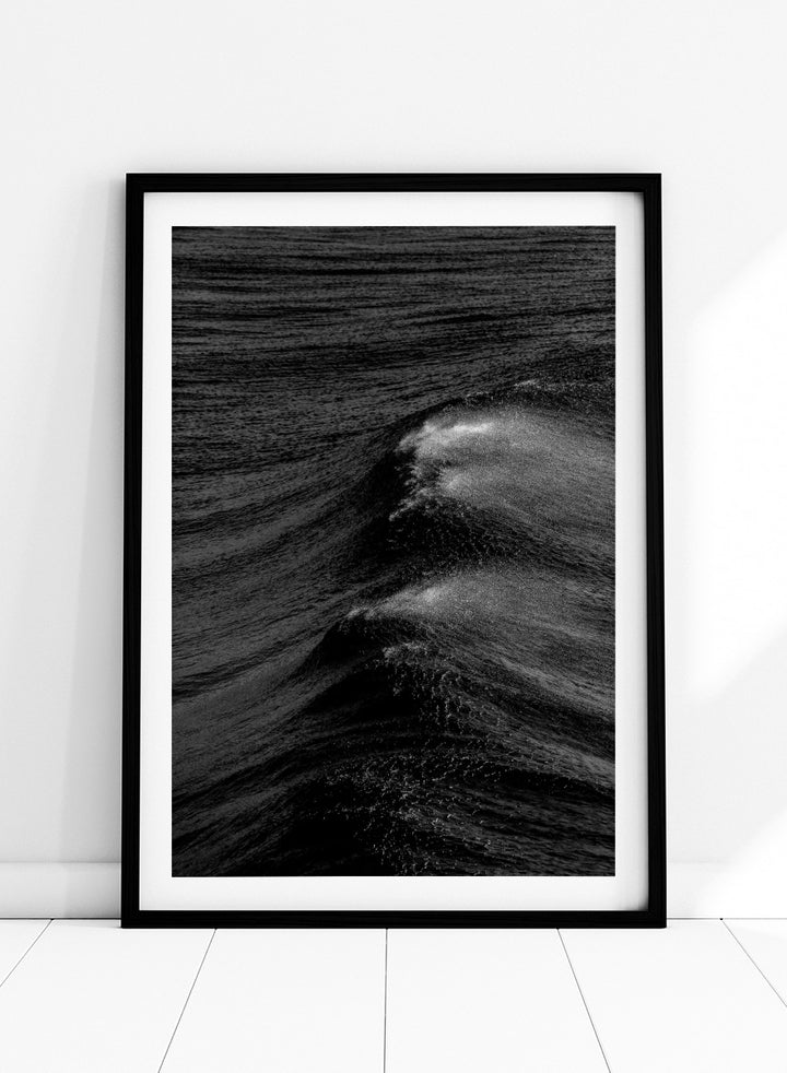 Black and white fine art photographic print of ocean waves, featuring a dramatic wave crest with white foam against dark textured water. Night Wave Cascade by Shot by Clint black-and-white ocean photography print featuring dark rolling waves, sea spray, and dramatic natural movement.