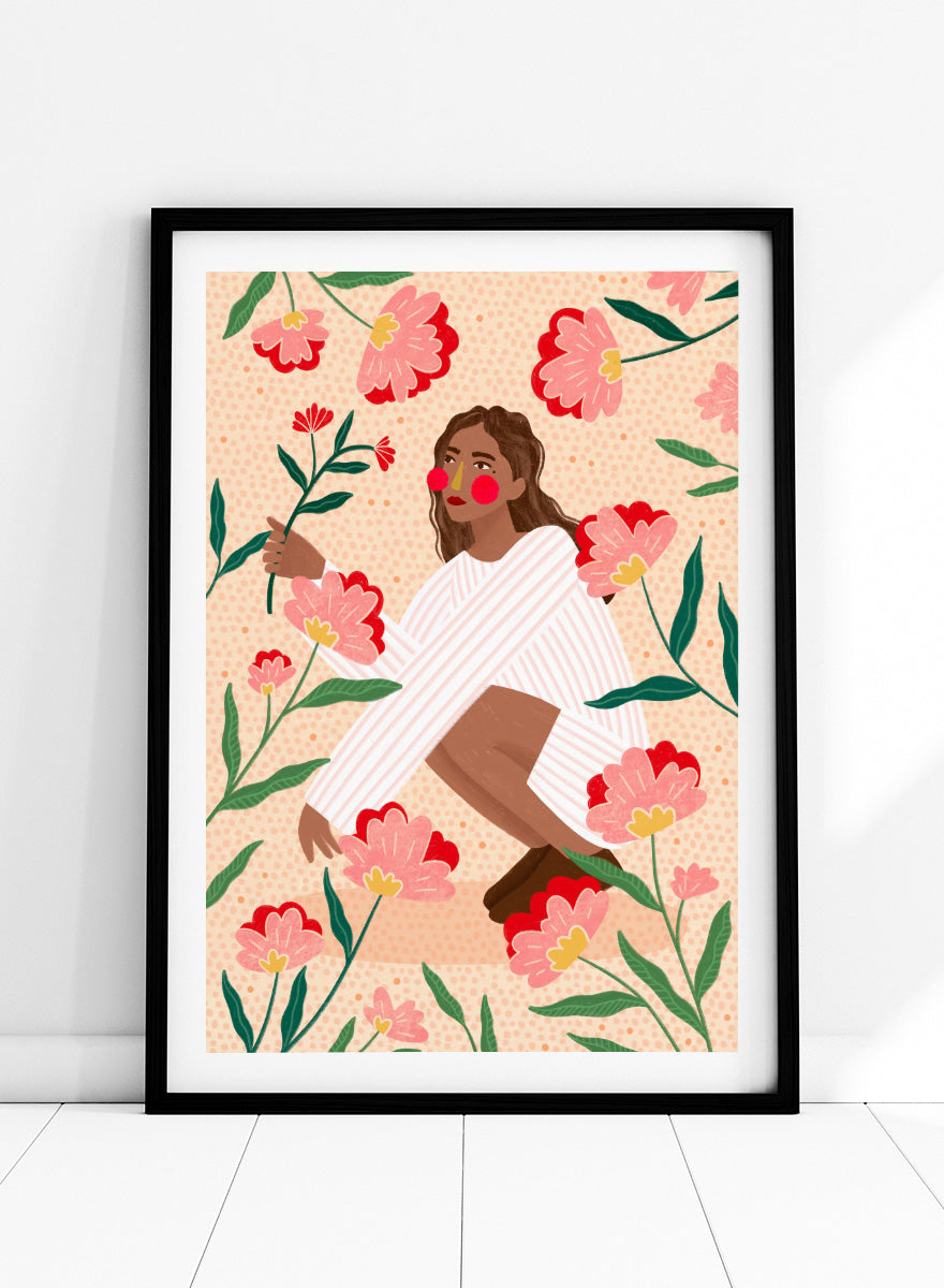A framed art print featuring a stylized illustration of a woman in a white striped sweater surrounded by pink and red flowers on a peach background. Woman in Floral Garden by Bea Müller floral art print featuring a woman surrounded by oversized pink flowers, green leaves, and playful botanical details.