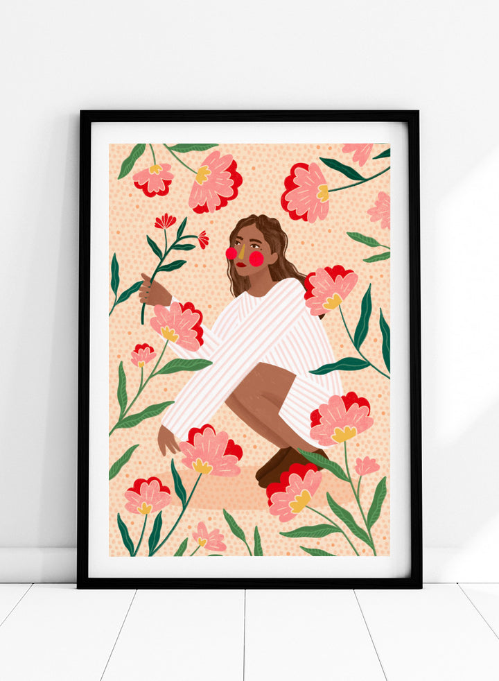A framed art print featuring a stylized illustration of a woman in a white striped sweater surrounded by pink and red flowers on a peach background. Woman in Floral Garden by Bea Müller floral art print featuring a woman surrounded by oversized pink flowers, green leaves, and playful botanical details.