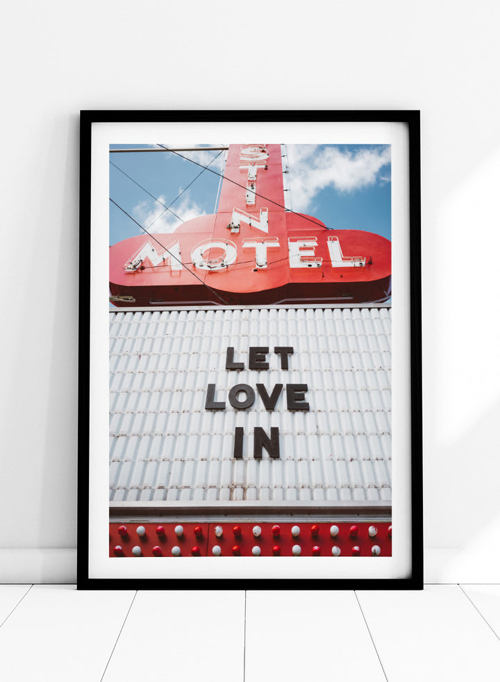 Vintage motel sign with 'Let Love In' message against a blue sky. Let Love In by Bethany Young features a vintage motel sign with red neon lettering against blue sky. Retro Americana photography wall art print.