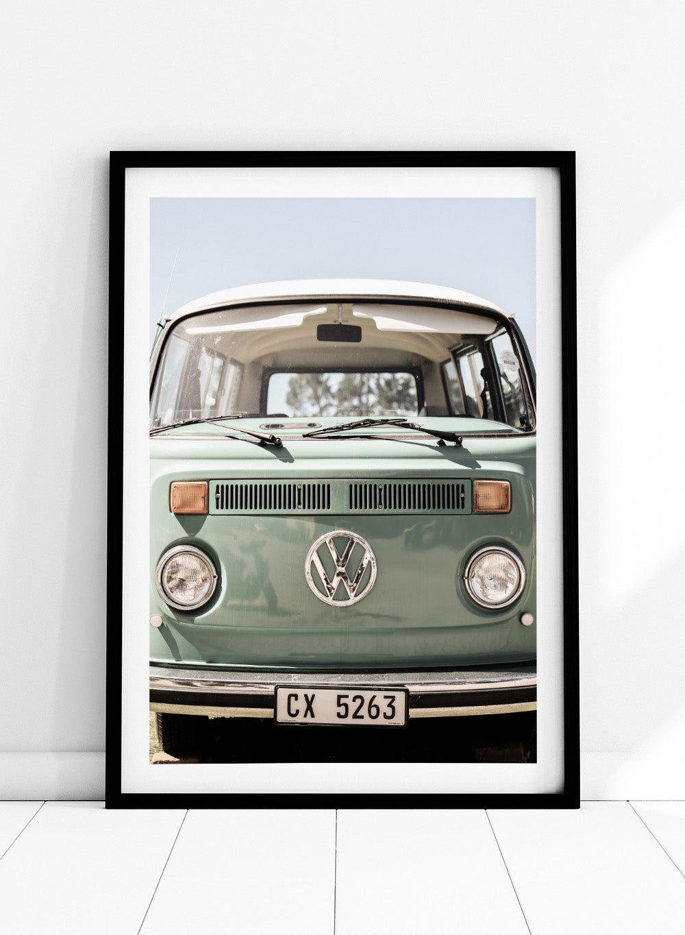 Front view of a vintage green Volkswagen van with clear sky background. Classic Design In Soft Green Tones by Shot by Clint car art print featuring a vintage Volkswagen camper van in soft sage green and warm sunlight.