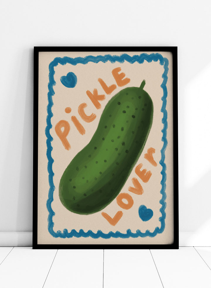 An art print featuring a hand-drawn green pickle centered on a cream background, surrounded by a blue scalloped border. The words &