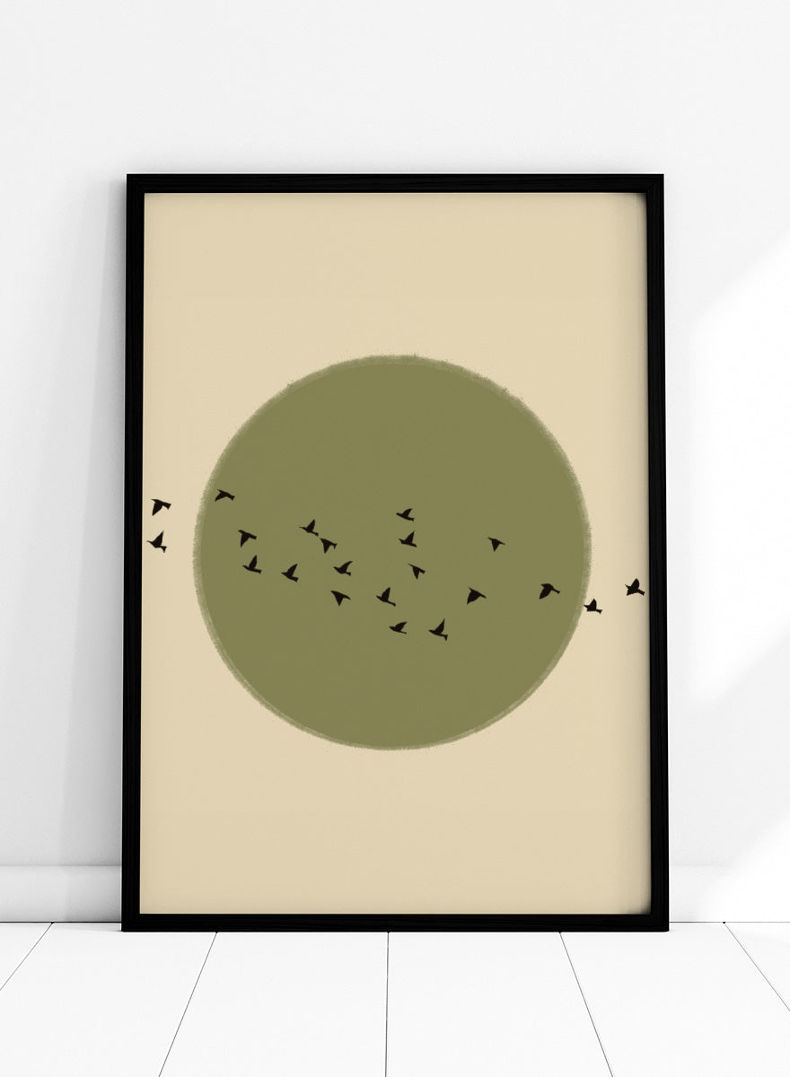 Minimalist art print featuring a large olive green circle with small black bird silhouettes flying across it, set against a warm beige background. Graceful Birds Soaring by The Art Concept is a minimalist bird art print featuring black birds in flight across an olive green circle and warm cream background.