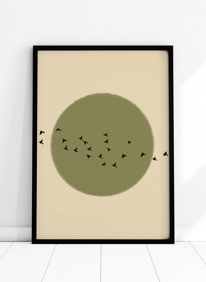 Minimalist art print featuring a large olive green circle with small black bird silhouettes flying across it, set against a warm beige background. Graceful Birds Soaring by The Art Concept is a minimalist bird art print featuring black birds in flight across an olive green circle and warm cream background.